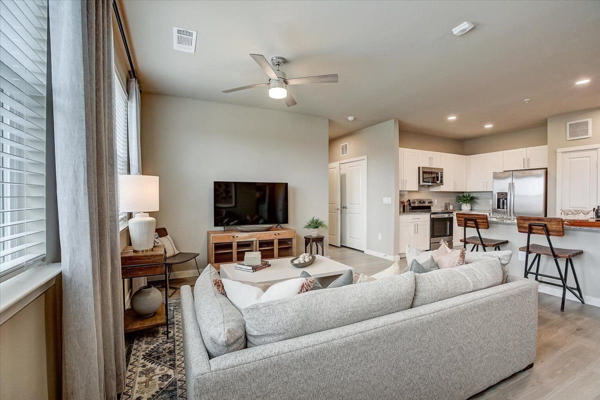 Living room with ceiling fan, media console, and breakfast bar connecting to the kitchen.